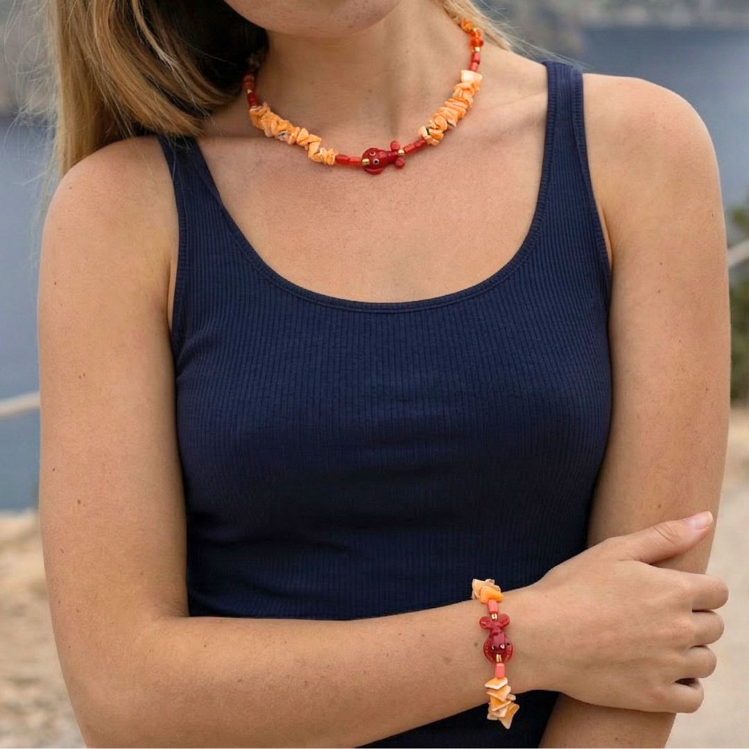 Oranje schelpenketting en oranje schelpen kralenarmband met rode kreeft bedel gedragen als set door model.
