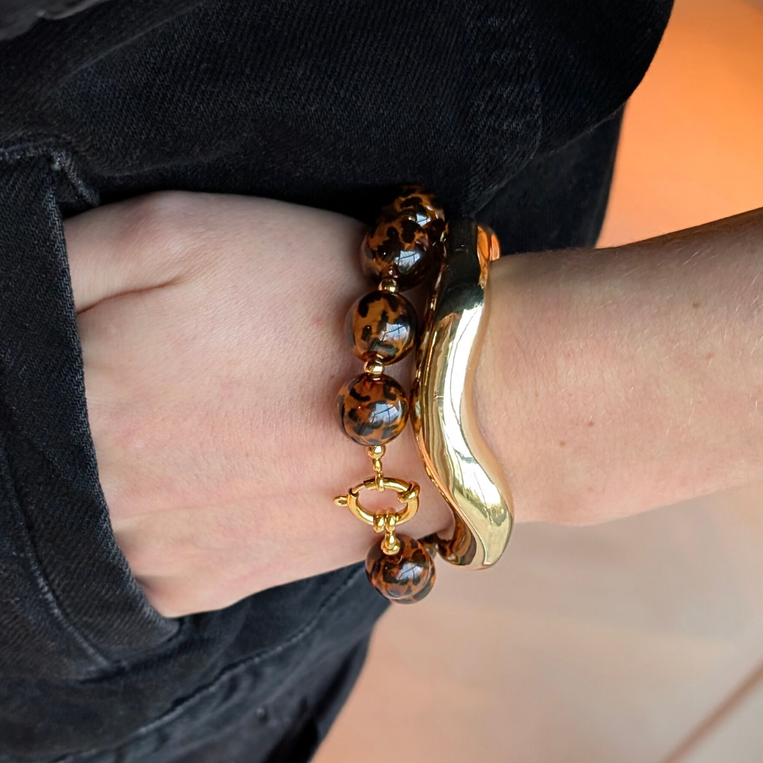Amber-bruine panter kralenarmband met ronde glanzende kralen en gouden sluiting, gecombineerd met een gouden bangle.