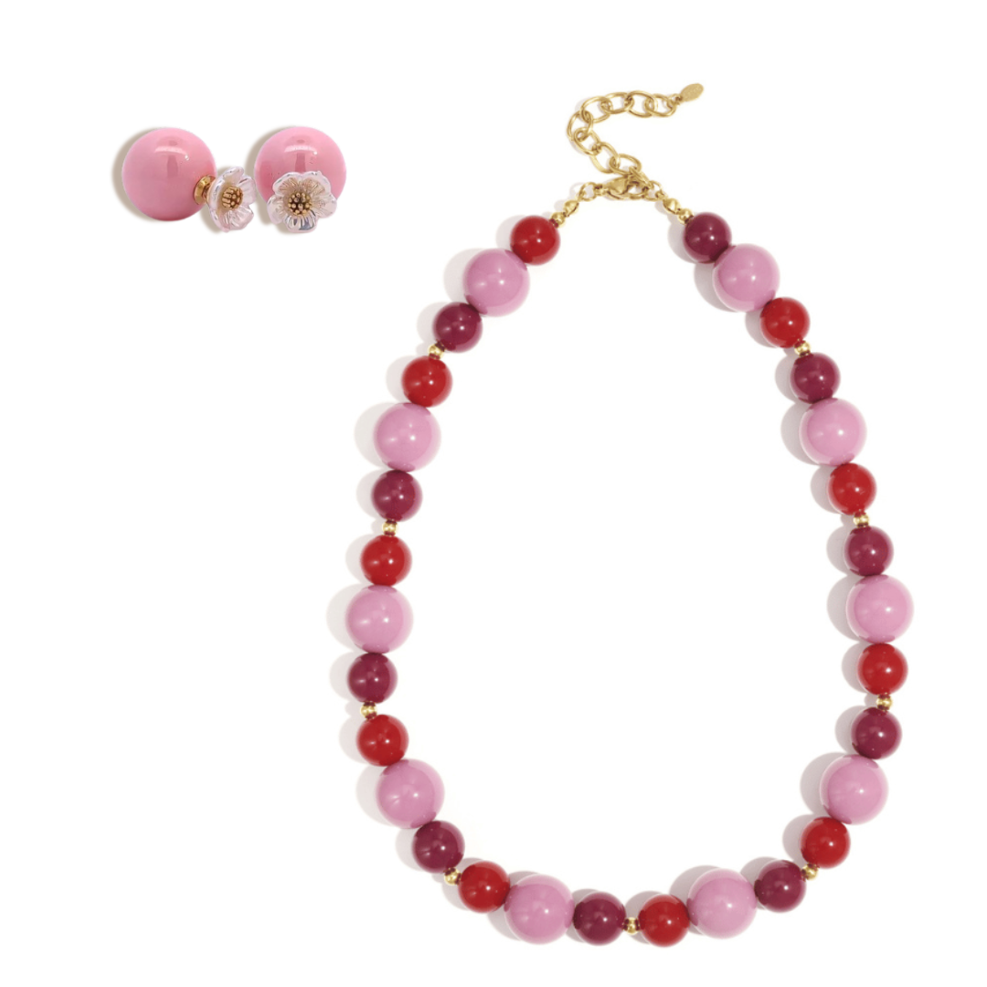 Roze en rode kralenset met ronde glanzende kralen en bloemvormige oorbellen met gouden details.