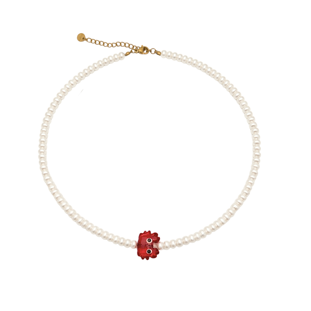 Parel kralenketting met kleine witte parelkralen en rode krabbedel op lichte achtergrond