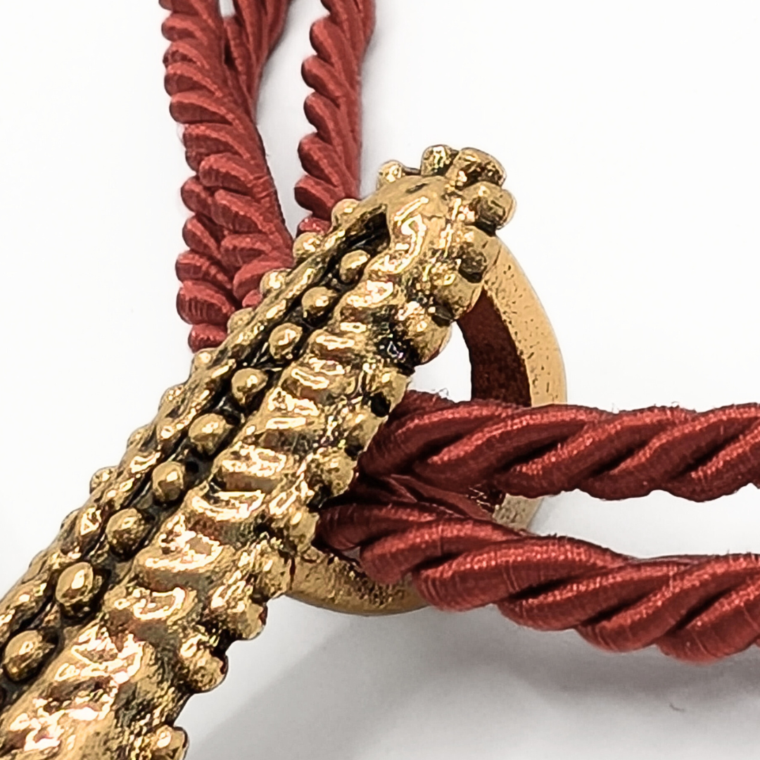 Detail van gouden zeester hanger bevestigd aan rode rope ketting