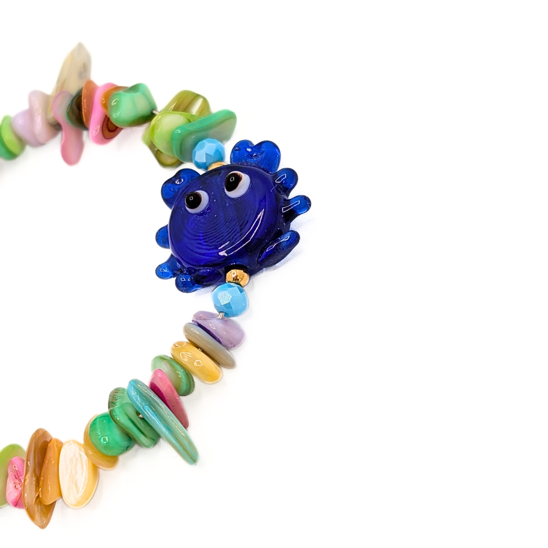 Detail van schelpen kralenarmband met blauwe glazen krab en pastel schelpkralen