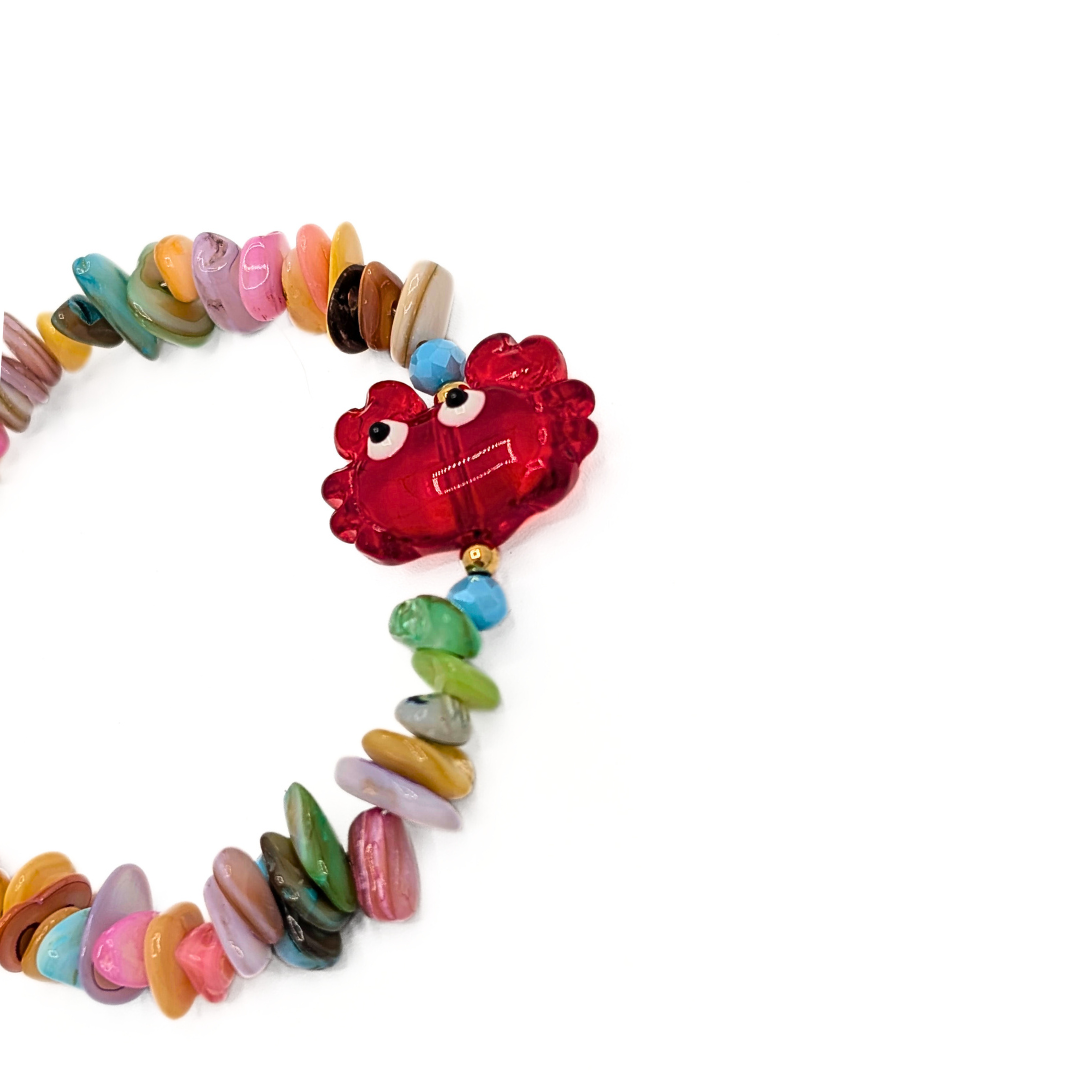 Detail van schelpen kralenarmband met rode glazen krab en pastel schelpkralen