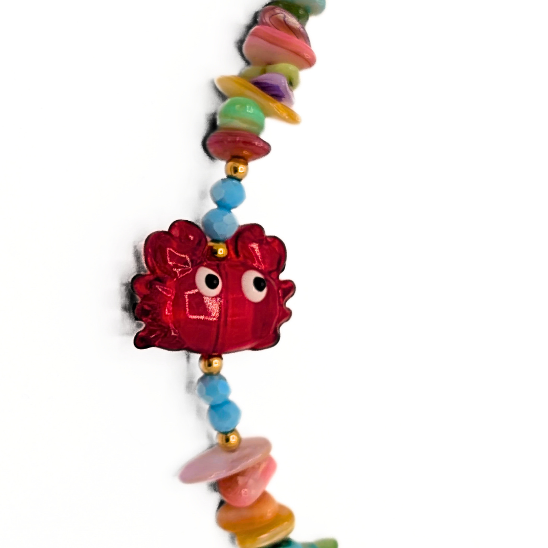 Detail van rode krab bedel aan multicolor schelpen kralenketting met blauwe kralen