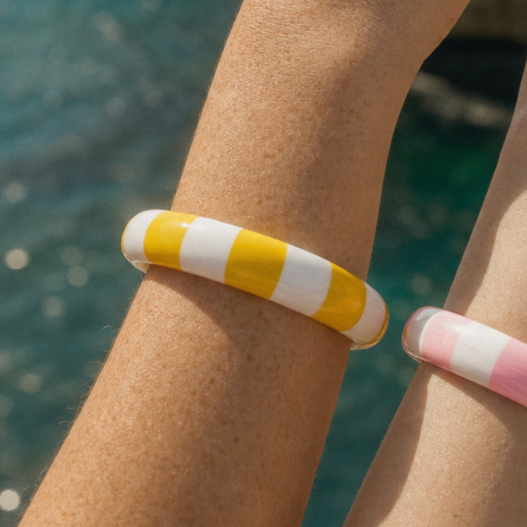 Geel-witte en roze-witte gestreepte candy bangle armbanden gestapeld op arm bij zee - Casa Jadel bangles
