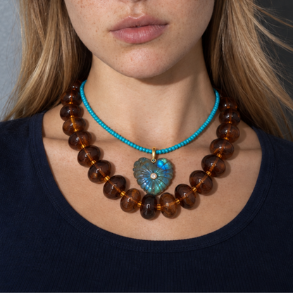 Model draagt een turquoise ketting met labradoriet hart boven een chunky amberbruine kralenketting.
