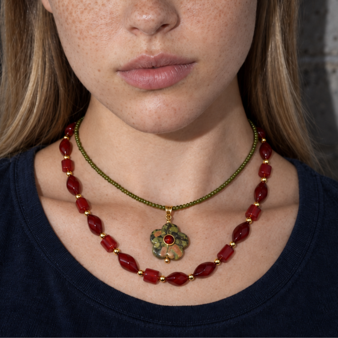 Model draagt een rode kralenketting en een fijne olijfgroene ketting met een unakiet bloemhanger.