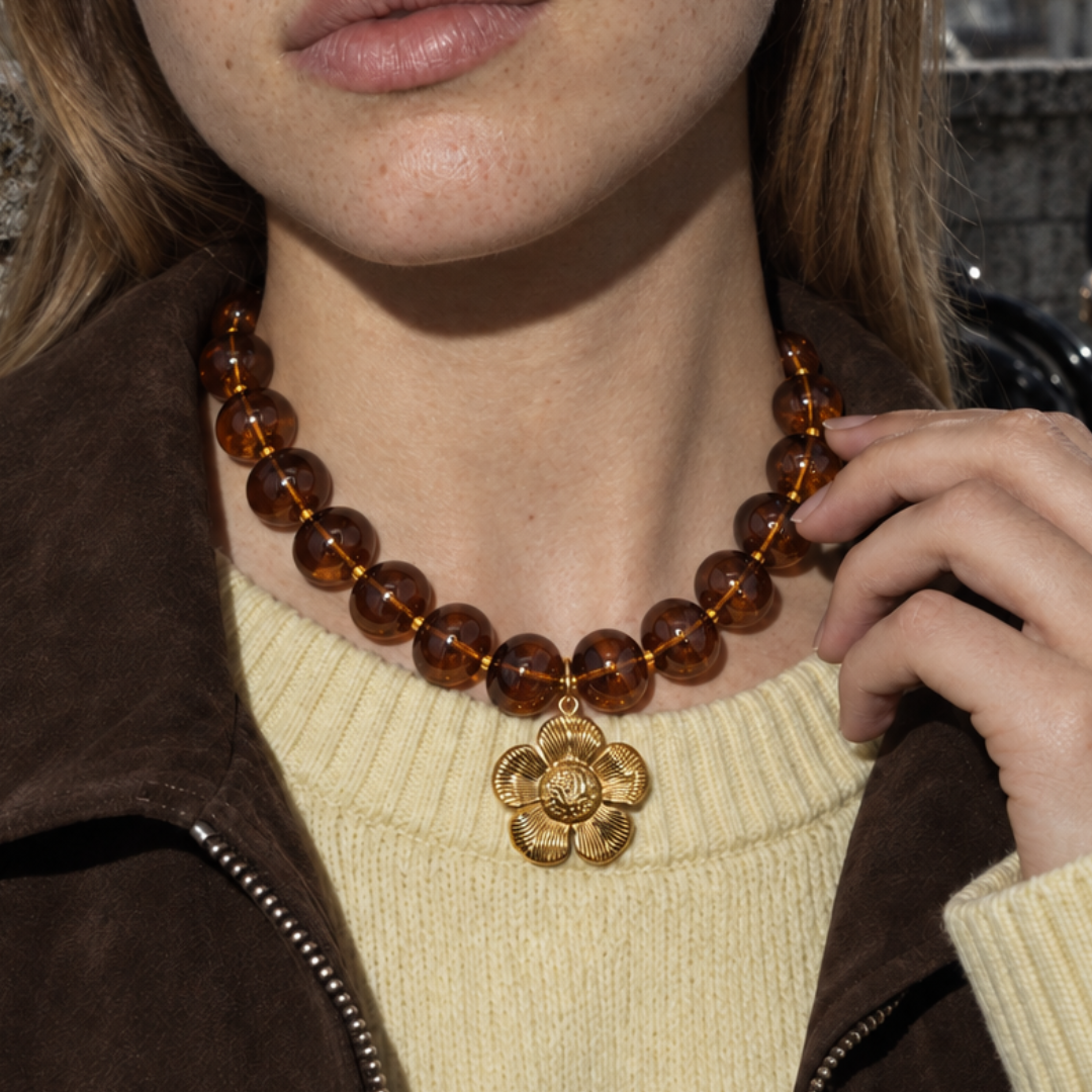 Amberkleurige kralenketting met gouden bloem hanger over gebreide trui - Casa Jadel
