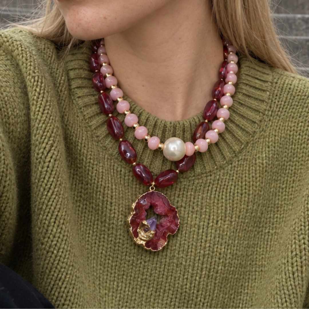 Model draagt een roze en burgundy kettingset met een grote natuursteen hanger over een groene trui.