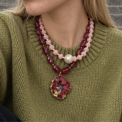 Model draagt een roze en burgundy kettingset met een grote natuursteen hanger over een groene trui.