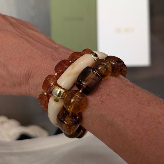 Amber bruine kralenarmband met gemarmerde amberlook kralen en ivoorkleurige details met goudaccent, gedragen om de pols – stijlvolle Ibiza-style armband van Casa Jadel.