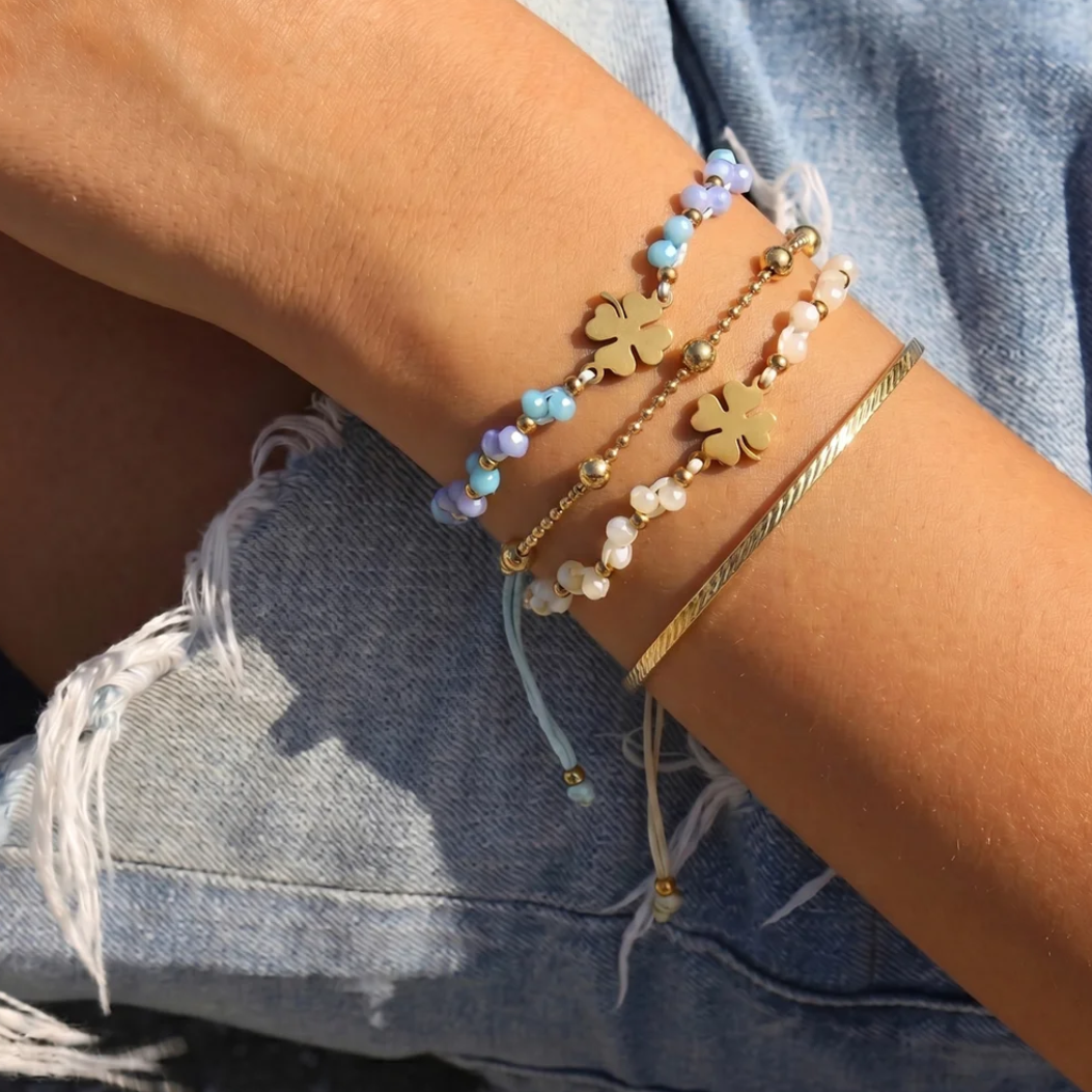 Arm met blauw en wit touw armbandje gouden klavertje kraaltjes