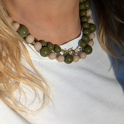 Beige en olijfgroene kralenketting met gouden accenten  en een legergroene kralenketting om de hals van een vrouw