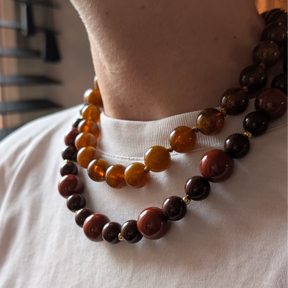 Chunky kralenkettingen in warme bruintinten, amber en chocoladebruin, met goudkleurige details, gedragen op een witte top.