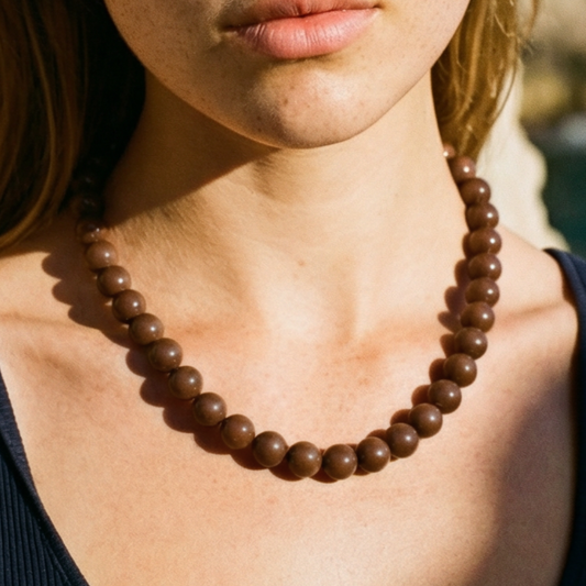 Bruine kralenketting met ronde glanzende kralen gedragen door model, minimalistische Ibiza style ketting in warme aardetint.