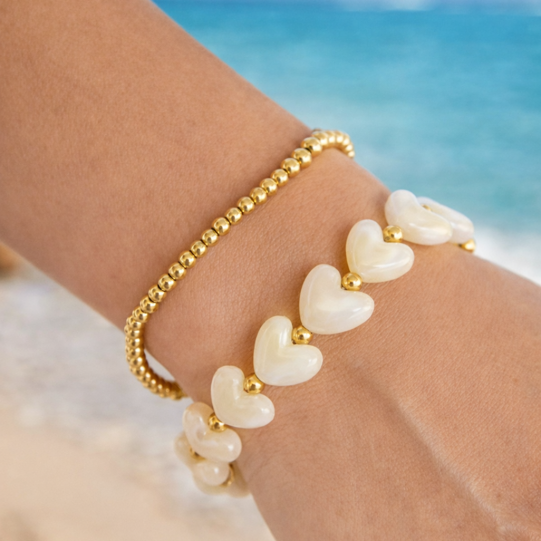 Arm met offwhite hartjes armband en gouden kraaltjes met goudkleurige details en zachte glans
