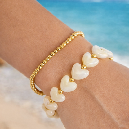 Arm met offwhite hartjes armband en gouden kraaltjes met goudkleurige details en zachte glans