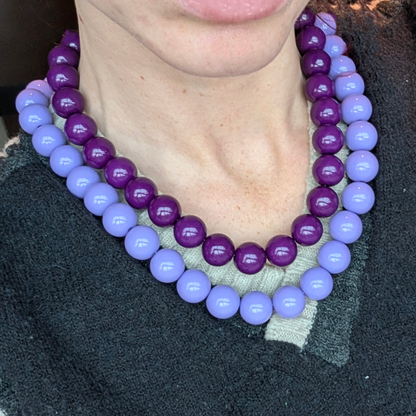 Dubbele paarse kralenketting met glanzende ronde kralen in lila en aubergine tinten, gedragen in een layered look.