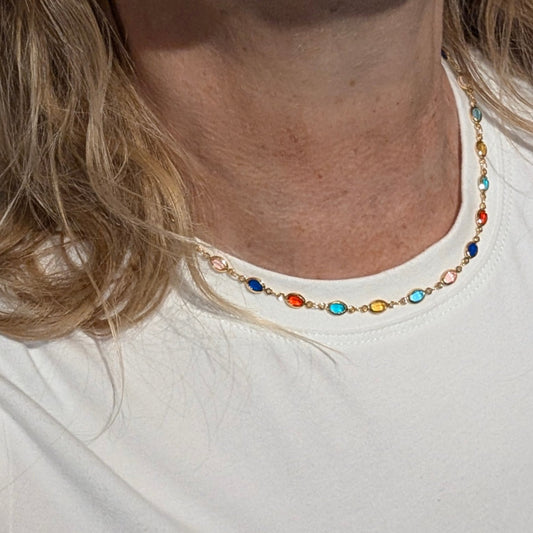 Goudkleurige ketting met kleine ovale gekleurde steentjes, subtiel gedragen op een witte top
