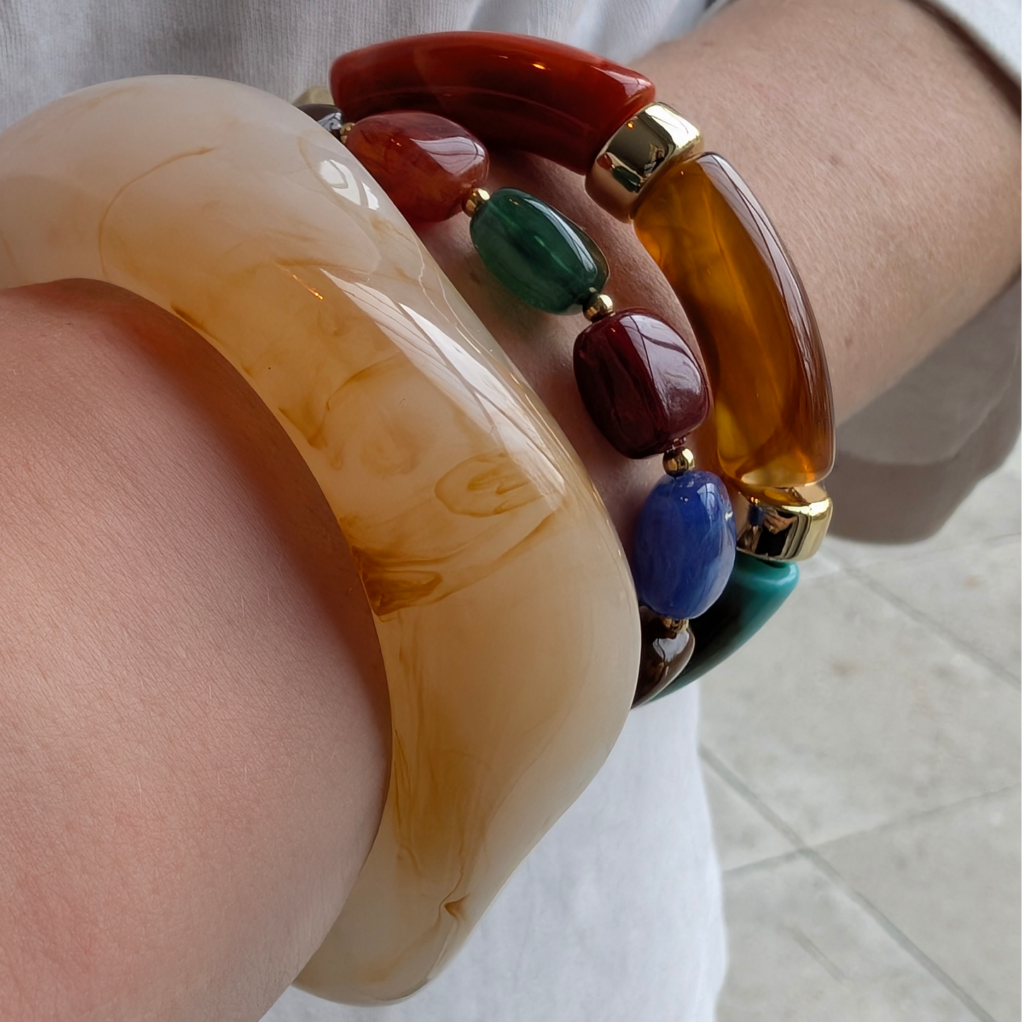Statement armbandenset met grote beige marmerlook bangle, gecombineerd met gekleurde chunky kralenarmbanden in rood, groen, blauw en amber.