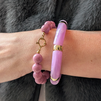 Lila armbanden set met glanzende ronde kralen plus een slotje en een chunky marmerlook  tube bangle met goudkleurige details, gedragen om de pols.
