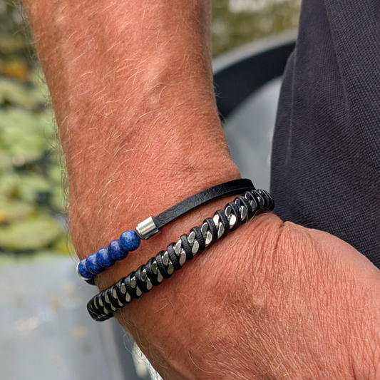 mannen arm met dubbele zwarte metalen armband en een armband met blauwe kraaltjes