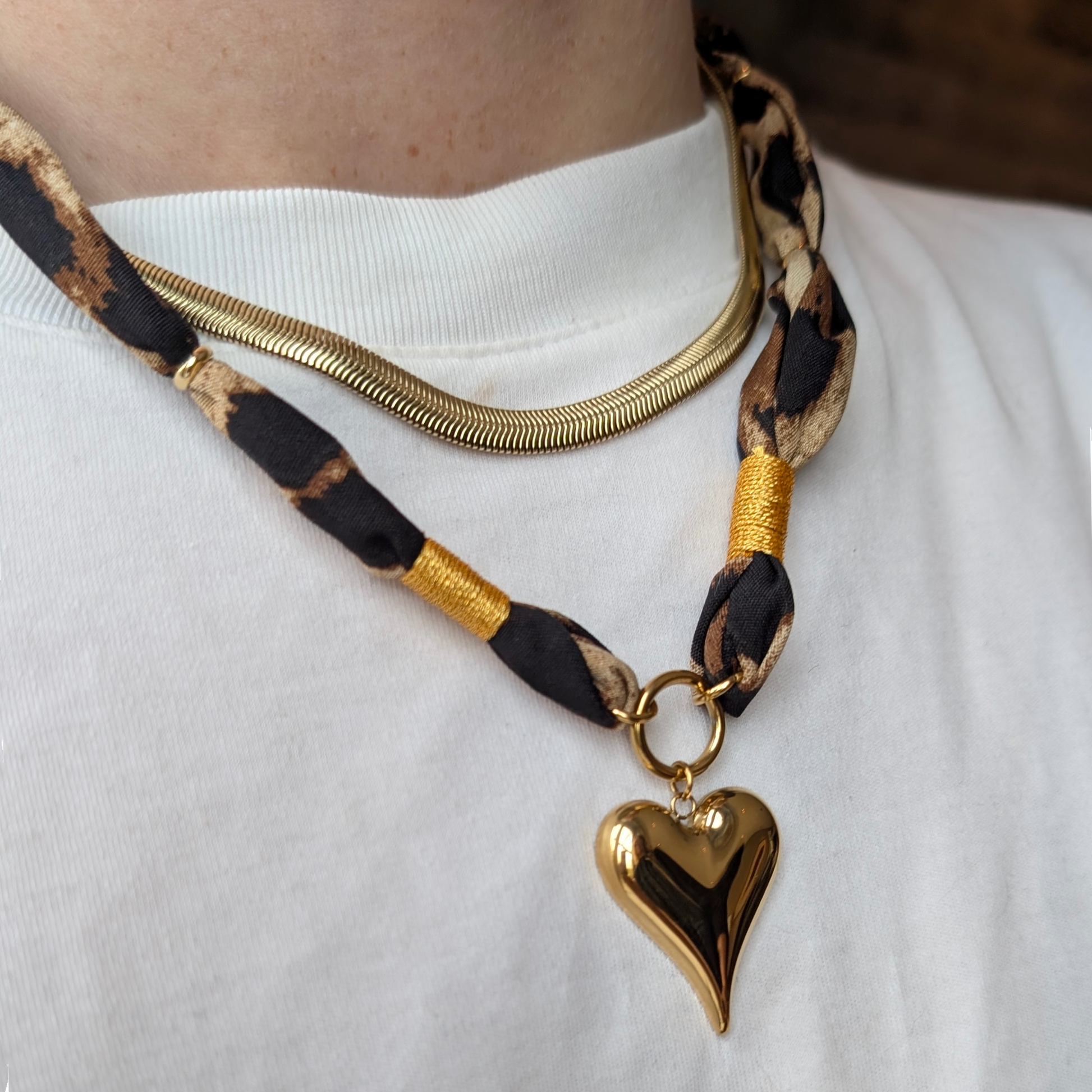 Stoere bandana-ketting met panterprint en goudaccenten, gecombineerd met een gouden hart-hanger en een chique goudkleurige snake chain.