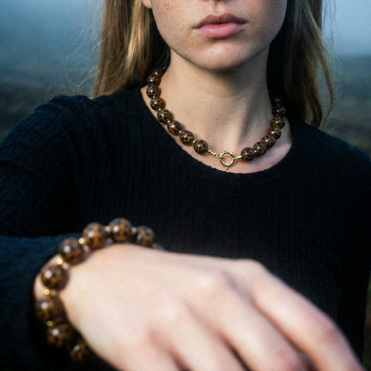 Ketting en armband met ronde kralen in panterprint, gedragen door model, sieradenset met goudkleurige boeislot en warme bruine tinten.