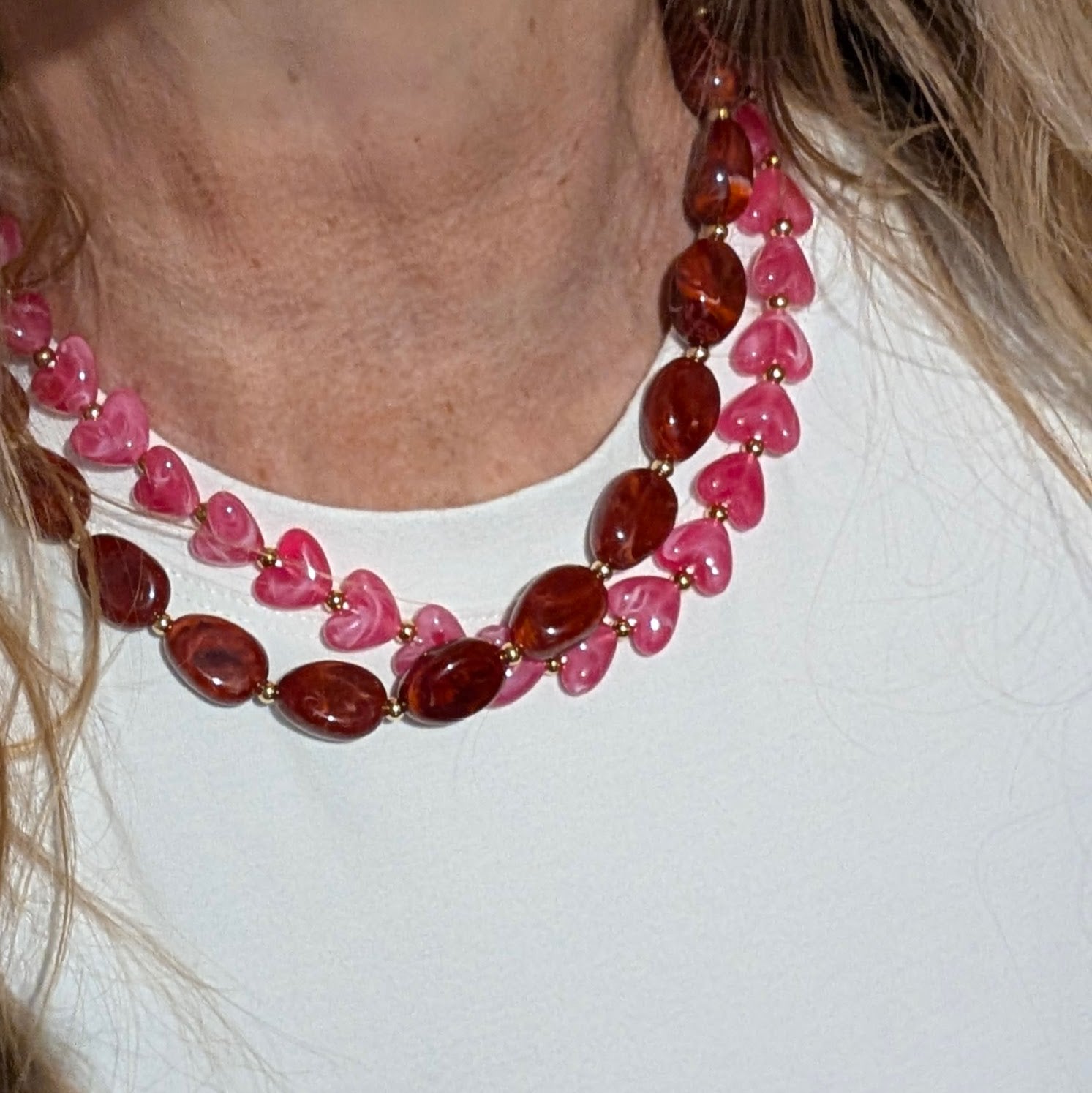 Rode gemarmerde kralenketting met ovale kralen en hartvormige kralenketting met goudkleurige tussenkralen op witte achtergrond