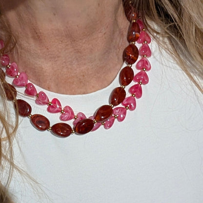 Rode gemarmerde kralenketting met ovale kralen en hartvormige kralenketting met goudkleurige tussenkralen op witte achtergrond