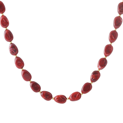 Rode gemarmerde kralenketting met goudkleurige details, gedragen op een witte top