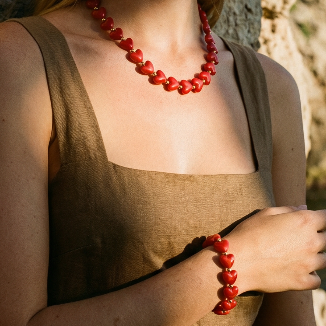 Rode hartjes ketting en armband set gedragen door model, sieraden met glanzende hartvormige kralen en goudkleurige details, zomerse Ibiza style uitstraling.
