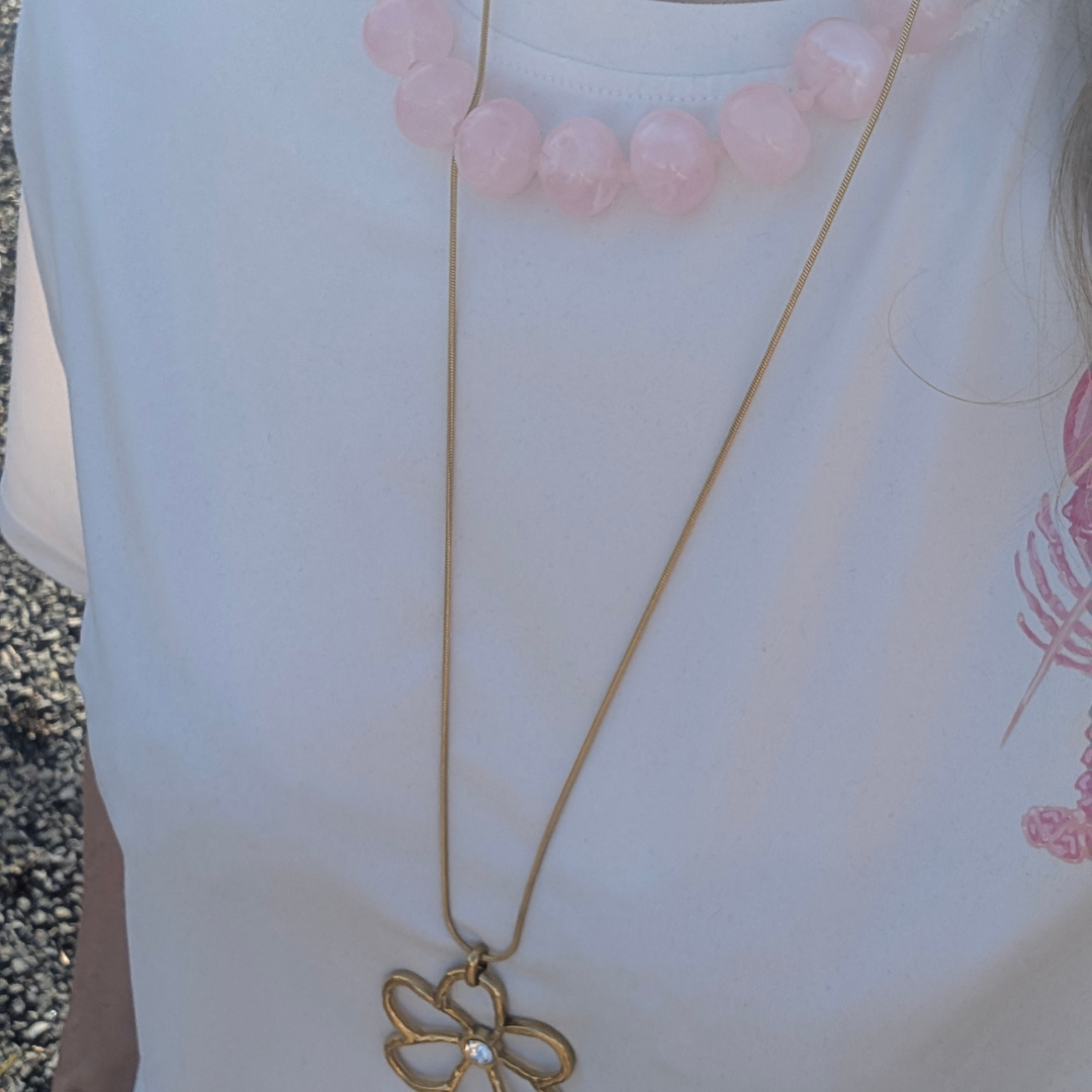 model met wit shirt met roze grote donut kralenketting en lange gouden bloemketting