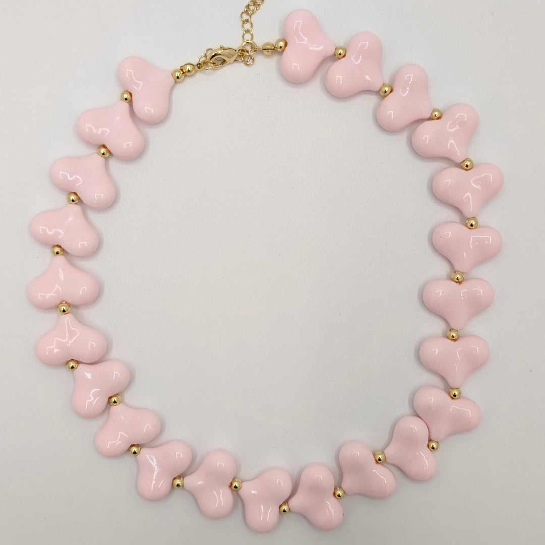 Lichtroze hartenketting met glanzende hartkralen en goudkleurige tussenkraaltjes.
