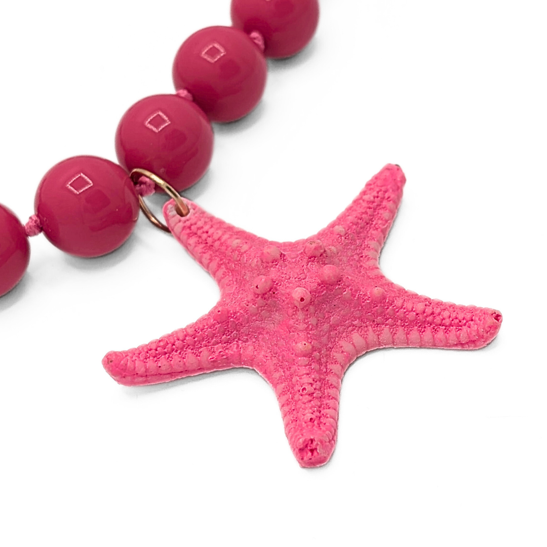 Detail van roze kralenketting met zeesterhanger en glanzende kralen
