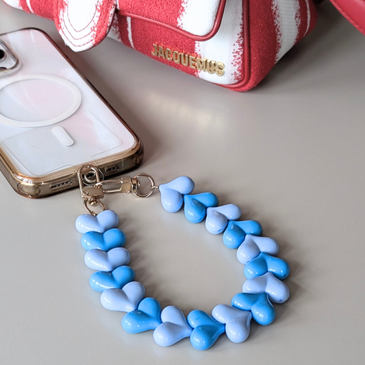 Telefoonkoord met hartvormige kralen in lichtblauw en blauw, duo hartjes design met goudkleurige clip, bevestigd aan smartphone.