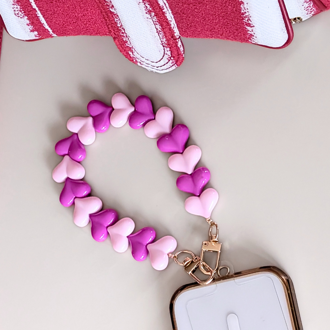 Telefoonkoord met hartvormige kralen in fuchsia en lichtroze, duo hartjes design met goudkleurige clip, bevestigd aan smartphone.