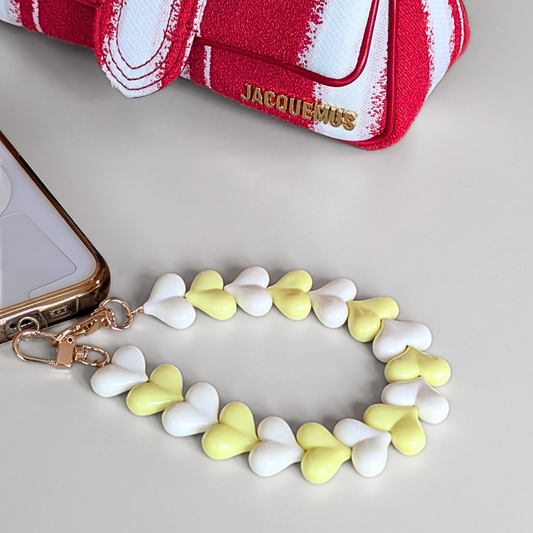 Telefoonkoord met hartvormige kralen in wit en pastelgeel, duo hartjes design met goudkleurige clip, bevestigd aan smartphone.