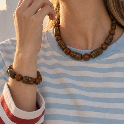 Model in gestreepte trui draagt de amber-bruine long & round marble kralenketting en bijpassende kralenarmband.