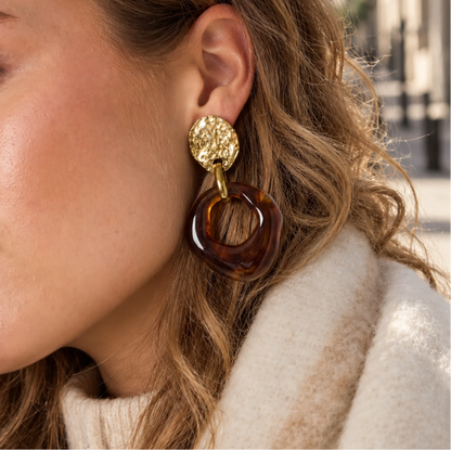 model met Amber bruine statement oorbellen met grote organische marble hanger en gouden details. Warme opvallende oorbellen voor iedere look.