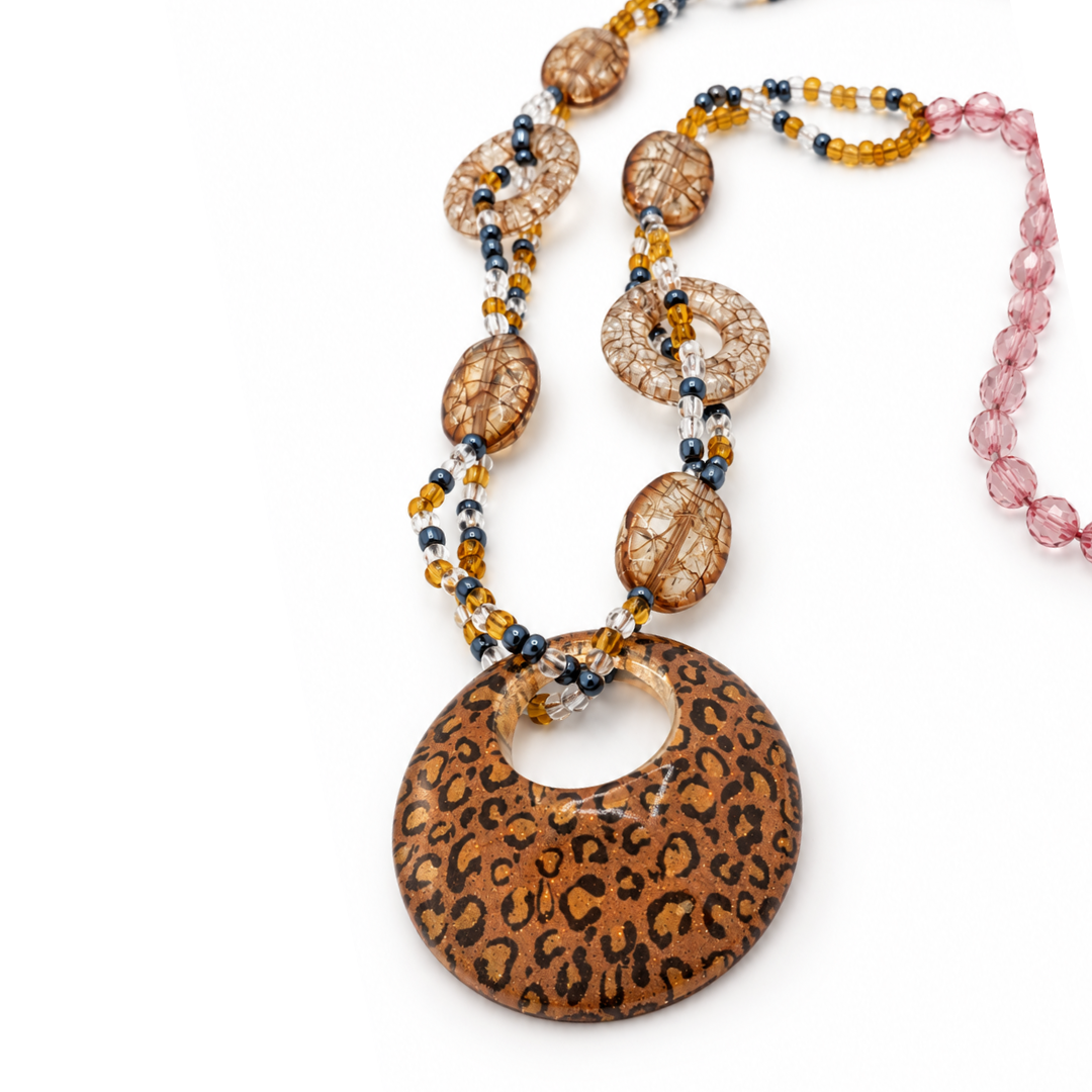 Schuin detail van de amberkleurige ketting met panterhanger, roze facetkralen en ovale en open ronde kralen met craquelé-effect.