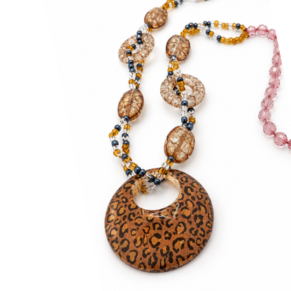 Schuin detail van de amberkleurige ketting met panterhanger, roze facetkralen en ovale en open ronde kralen met craquelé-effect.