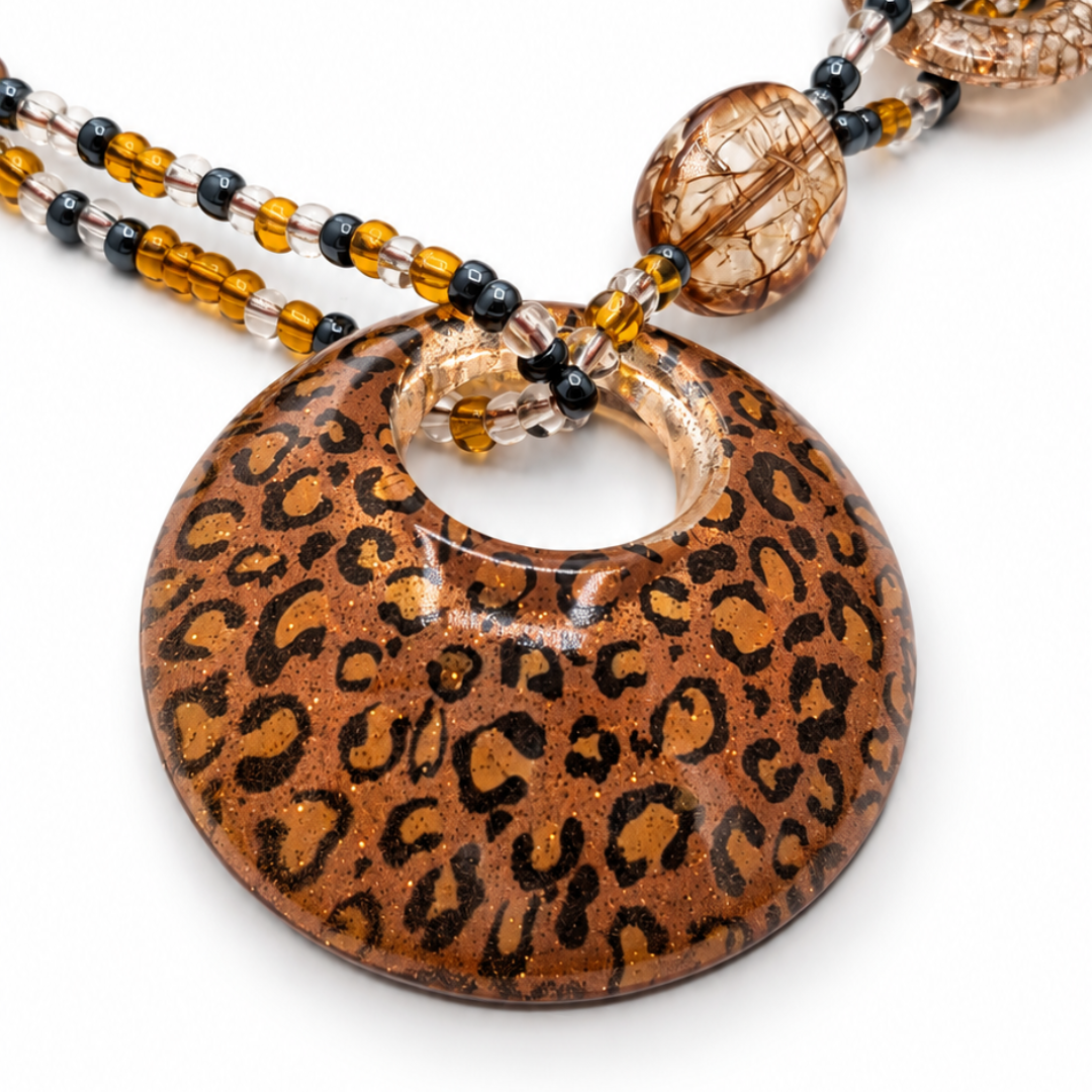Close-up van de ronde amberbruine panterhanger met zwarte vlekken en een ronde opening aan de mixed kralenketting.