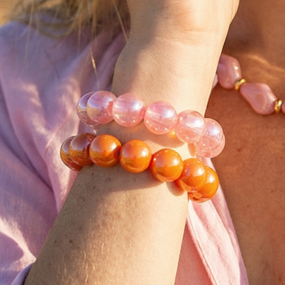 Arm met roze en oranje parelglans chunky kralenarmband met grote glanzende kralen op lichte achtergrond.
