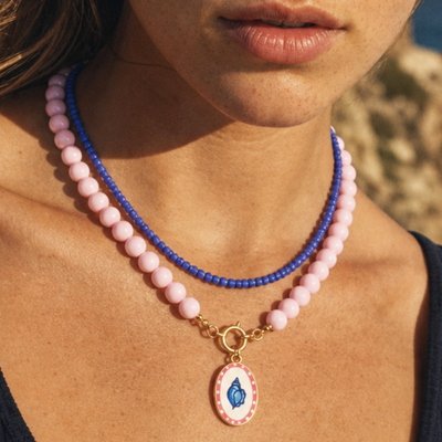 Model draagt de babyroze-blauwe kralenset met schelpbedel van Casa Jadel in een zomerse look.