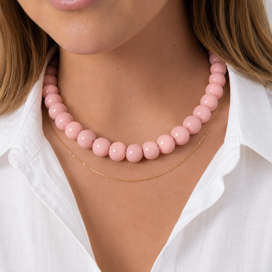 Model draagt lichtroze kralenketting met ronde kralen van Casa Jadel, samen met een eenvoudige gouden ketting