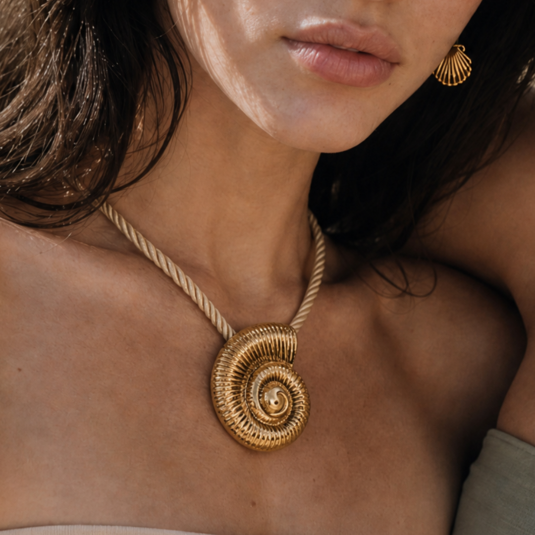 Model draagt een beige koordketting met grote goudkleurige schelp bedel en gouden schelp oorbel van Casa Jadel