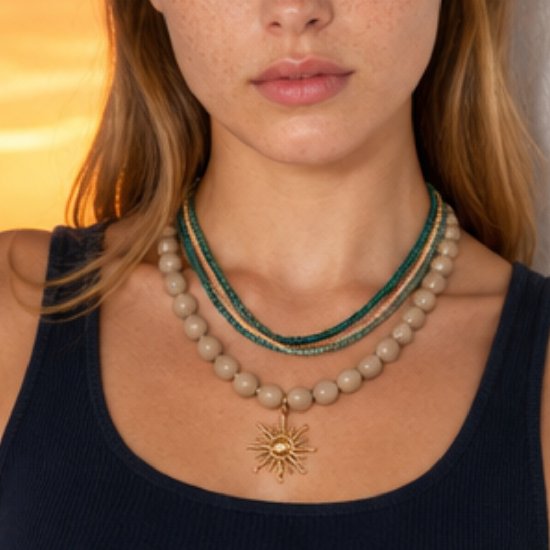Model draagt een beige kralenketting met goudkleurige zon bedel en turquoise kralenkettingen in laagjes van Casa Jadel