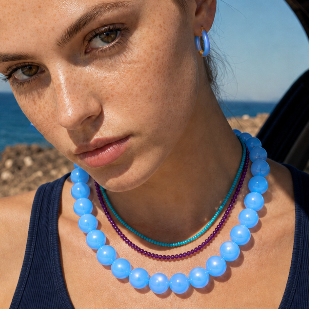 Model draagt een blauwe chunky kralenketting met paarse en turquoise kleine kralenkettingen in laagjes van Casa Jadel
