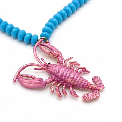 Close up van blauwe ovale lange kralenketting met roze kreeftbedel van Casa Jadel